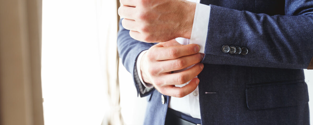 Cropped photo of an elegant young man buttoning up the sleeve of his white shirt