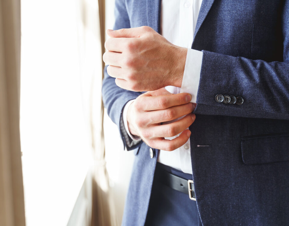 Cropped photo of an elegant young man buttoning up the sleeve of his white shirt